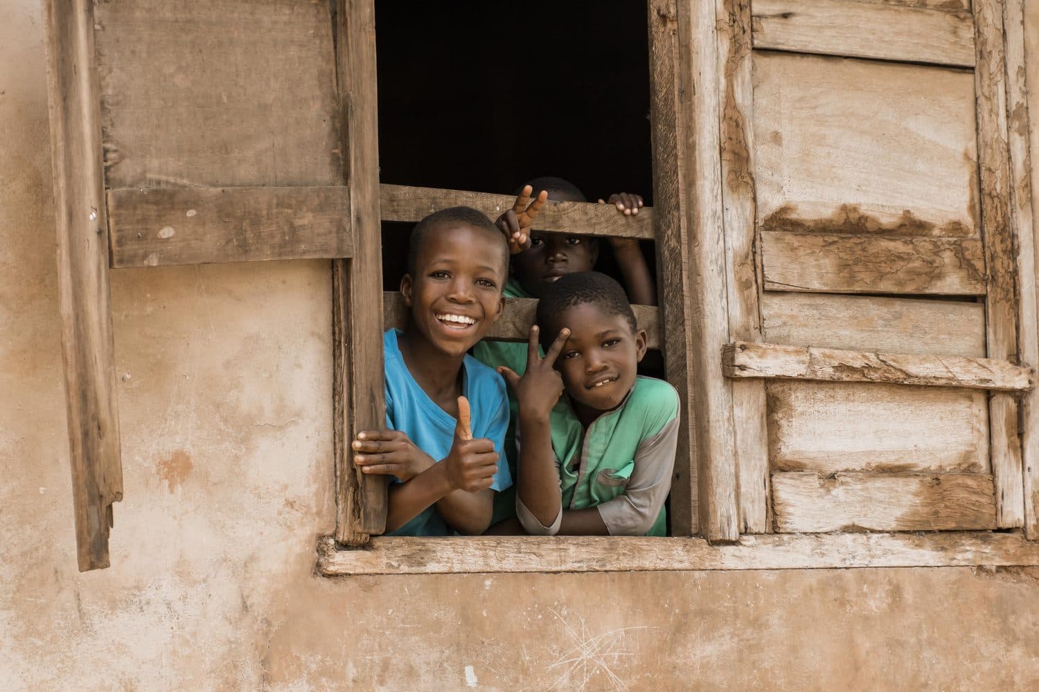 Two smiling children looking through a wooden window.