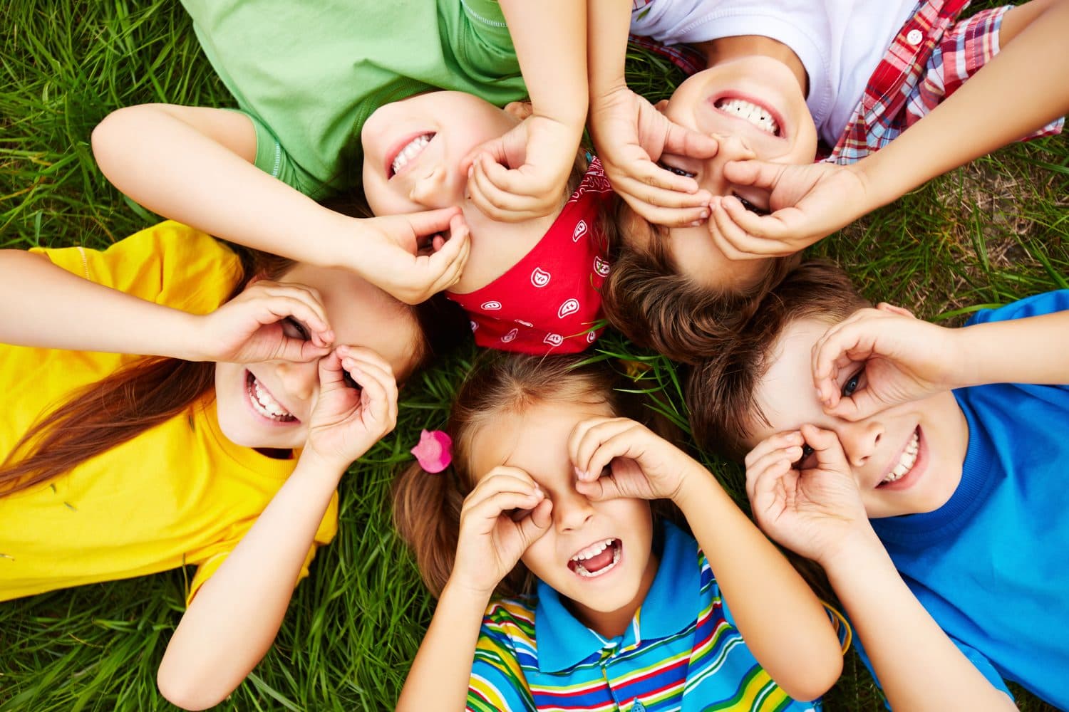 Children lying on grass and smiling up at the camera.